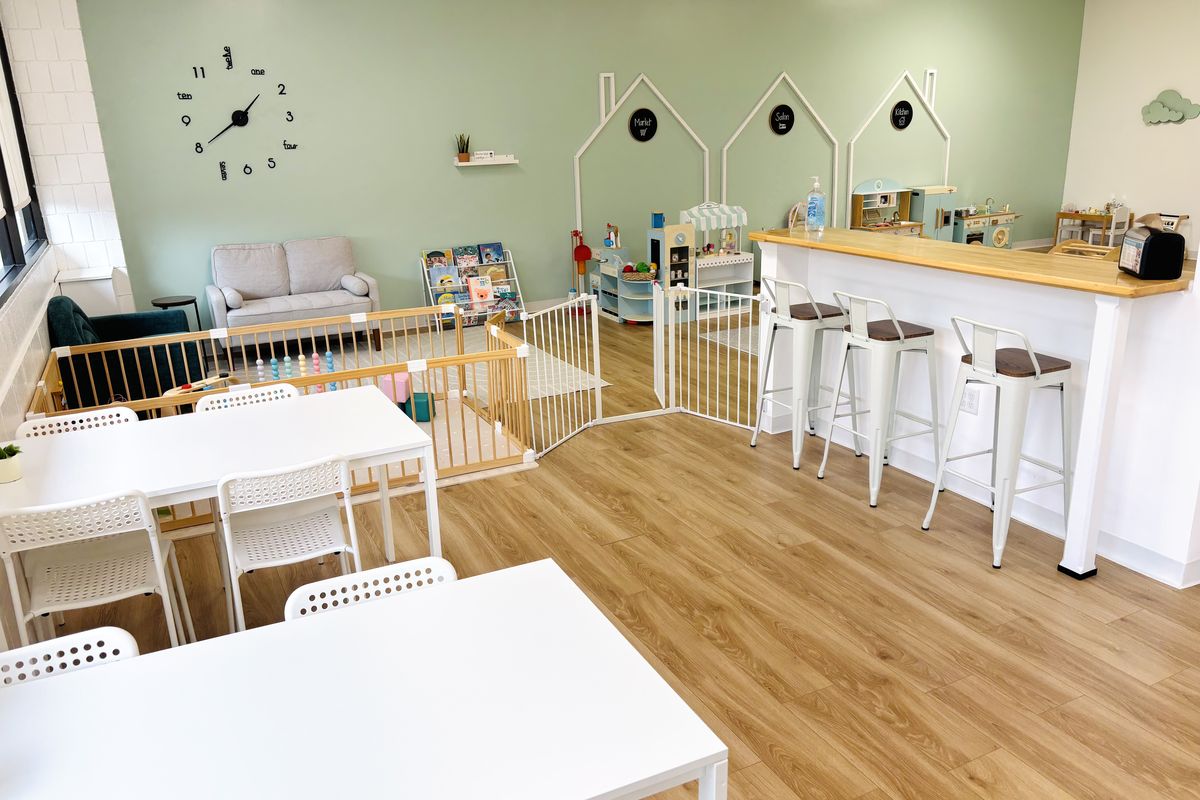 The café side: white tables and chairs, the butcher-block counter with stools, and the gated baby area and play floor just beyond.