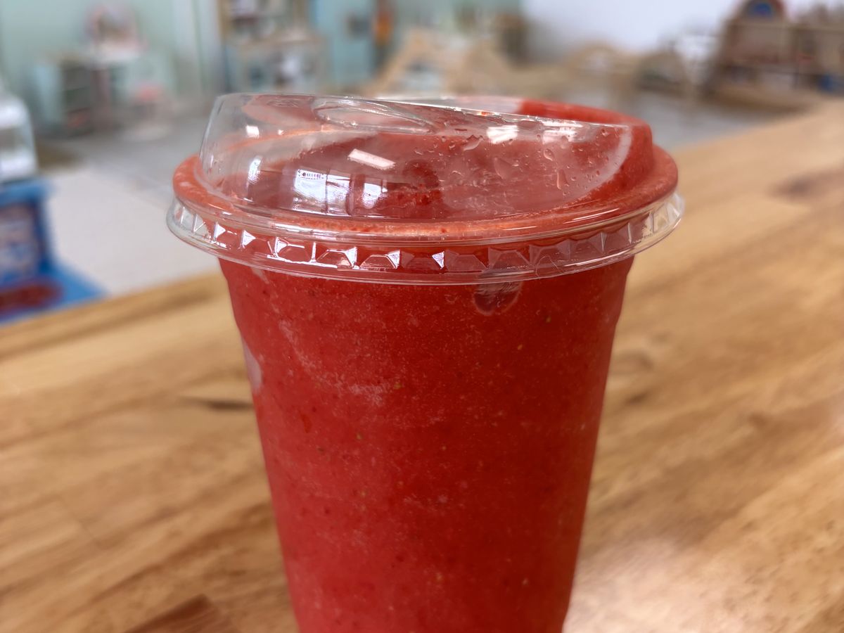 A red berry smoothie in a lidded cup on the café counter.