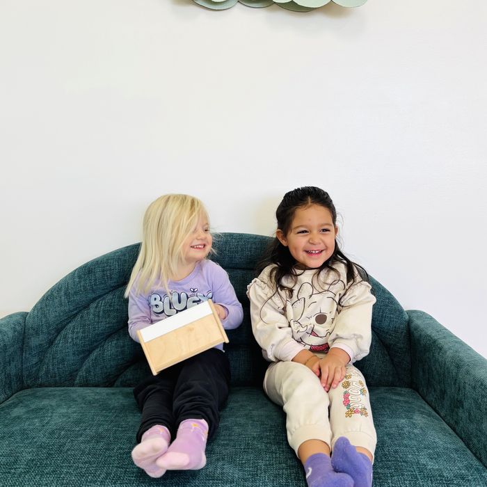 Two friends sitting together on a teal sofa, smiling.