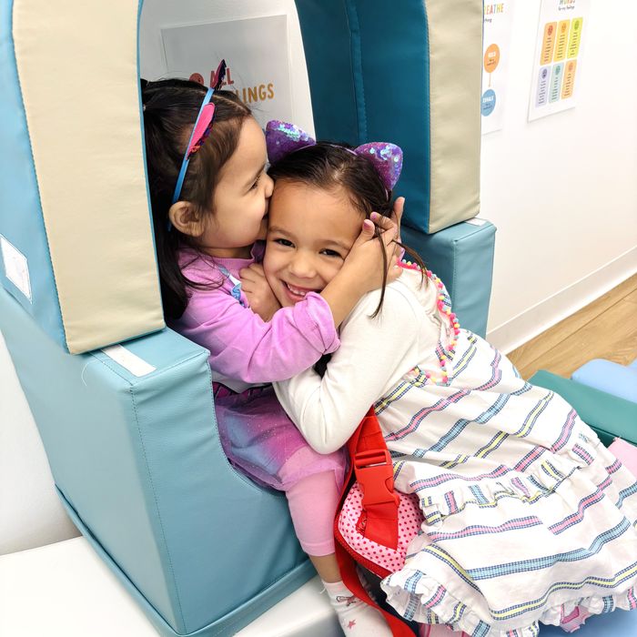 Two little girls hugging inside a soft-play arch.
