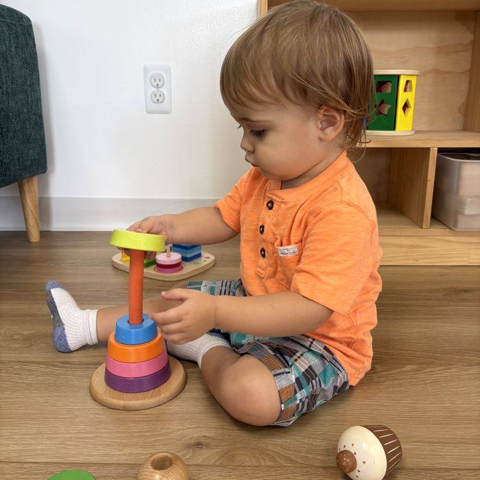 A toddler stacking rings on a wooden stacker on the floor.
