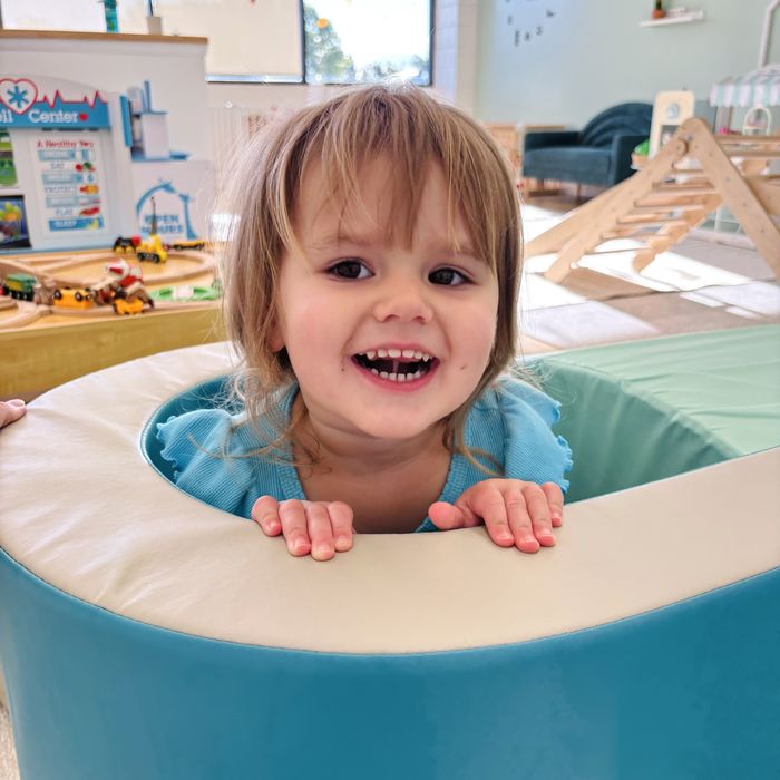 A smiling toddler peeking out of a soft ball-pit ring.