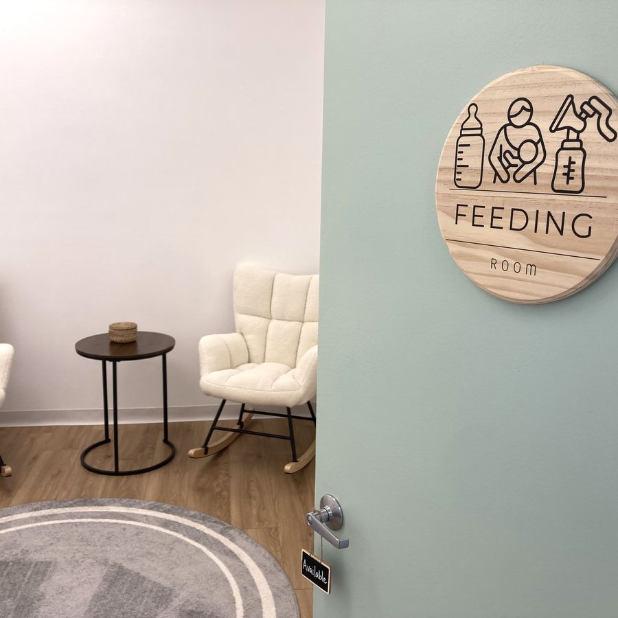 The feeding room: two cream rocking chairs with a small side table, a soft round rug and a lamp, behind a door marked Feeding Room.