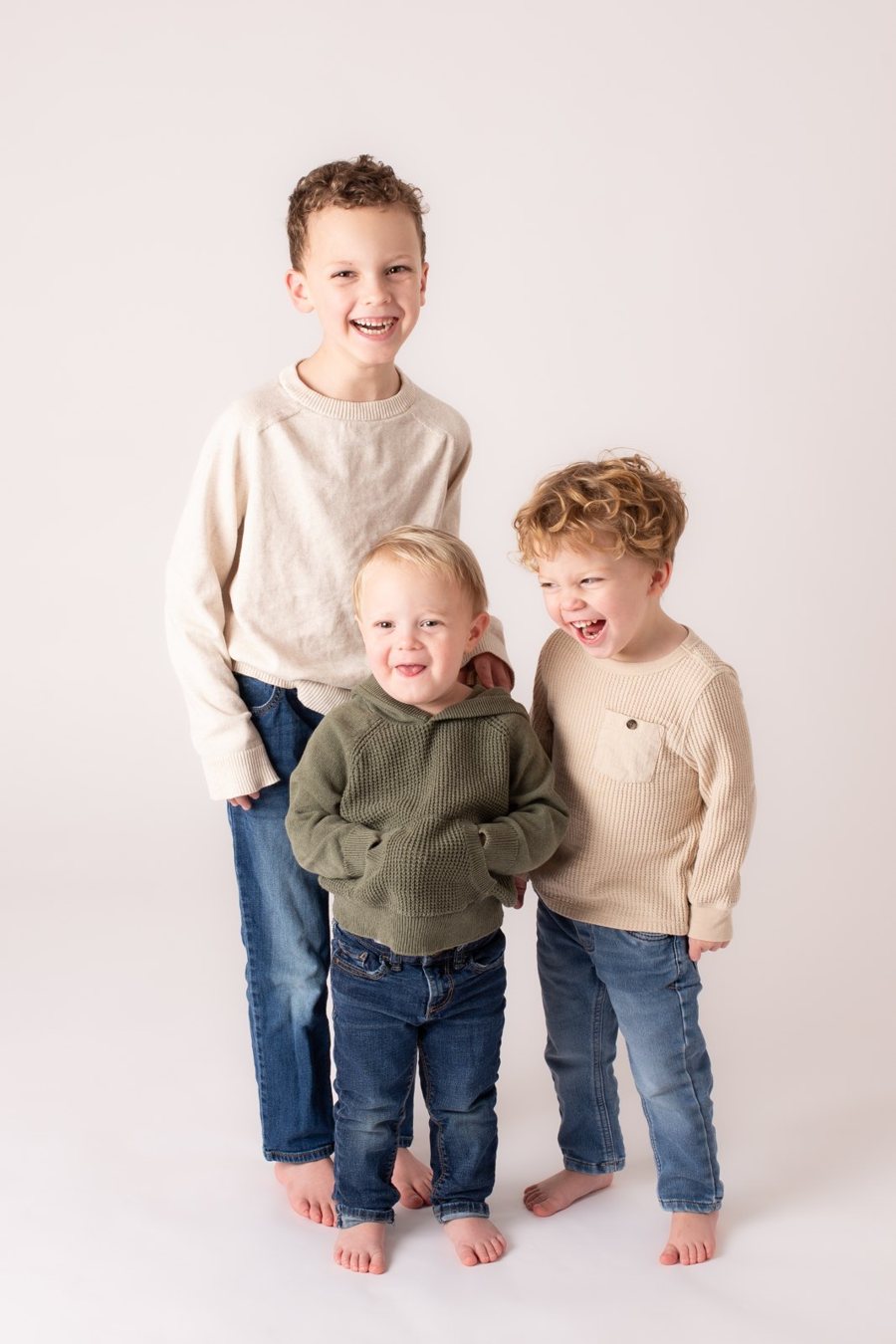 Three young cousins standing together barefoot and laughing in the studio.