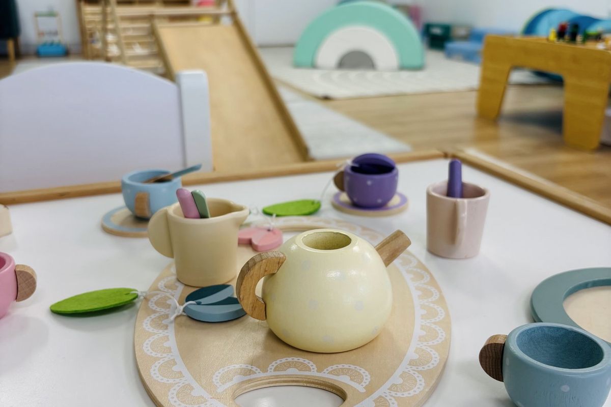 A pastel wooden tea set laid out on a small table in the play area.