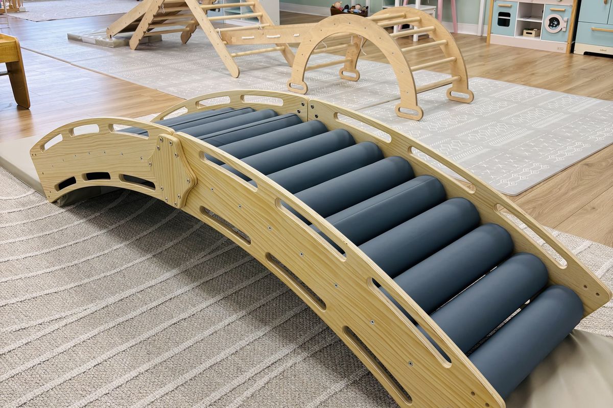 A wooden climbing bridge lined with soft teal-blue rollers, set on a cushioned mat in the play area.