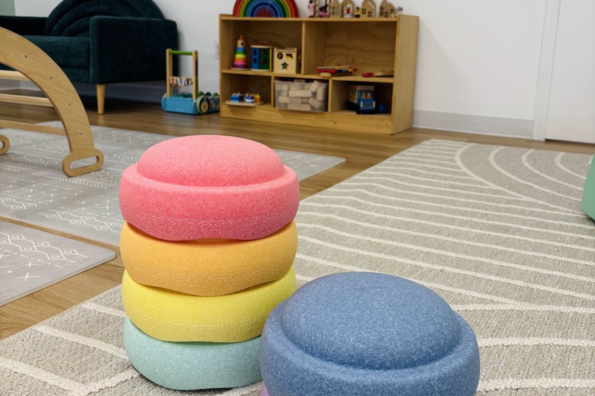 Rainbow stacking stones on a soft rug, with the teal sofa and toy shelves behind.