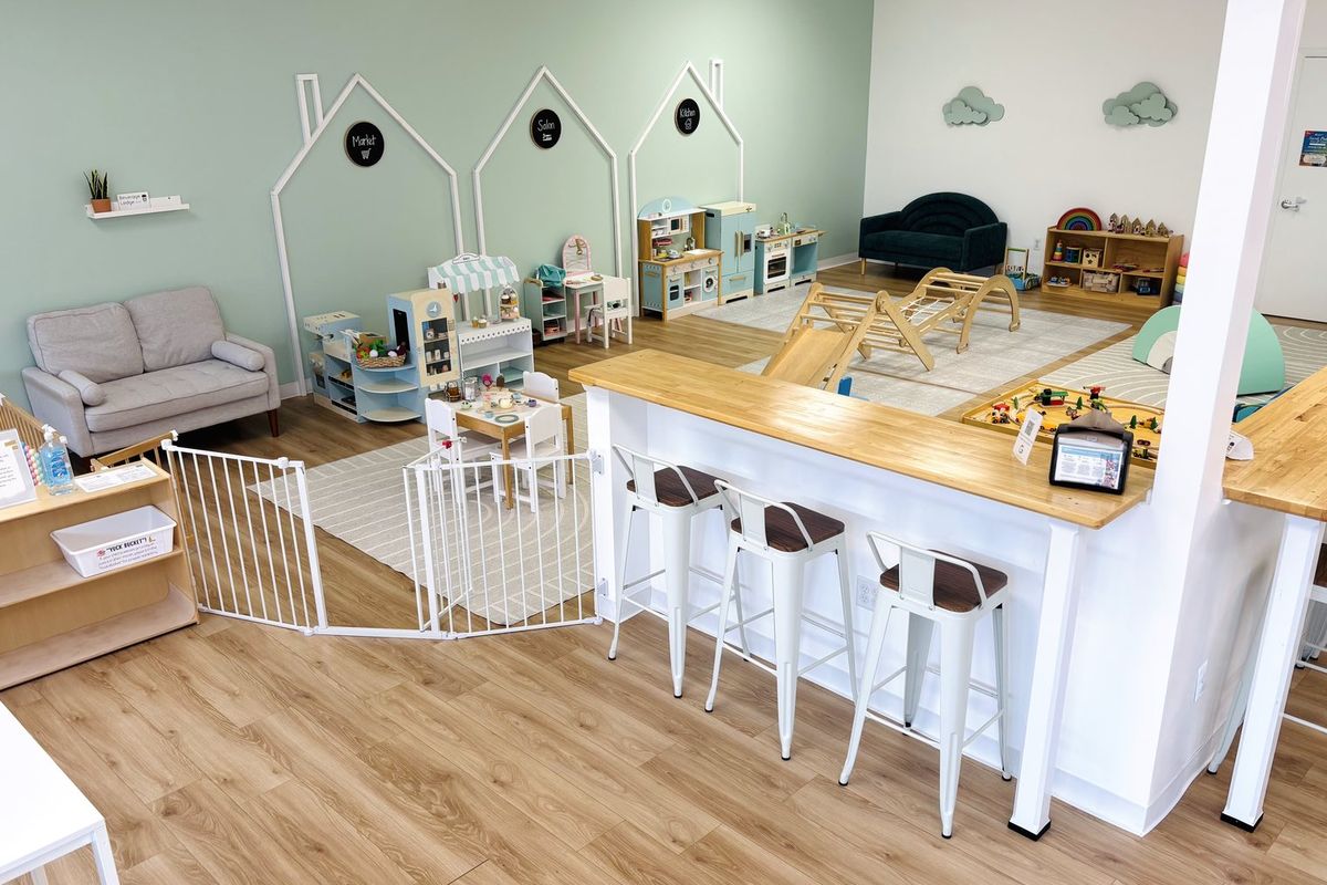 The cafe counter: a butcher-block bar with metal stools, looking across a low gate into the play area, with a sofa and bookshelves beyond.