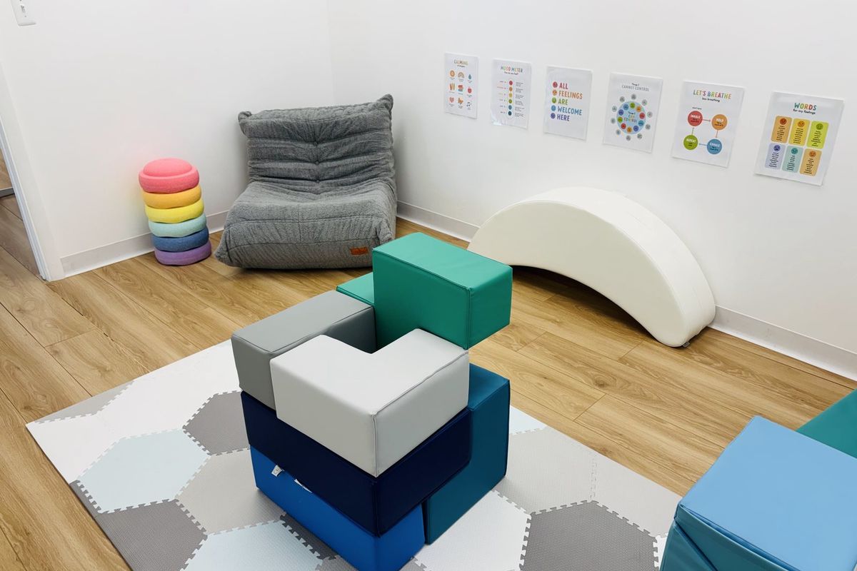 The mindfulness room: a grey bean-bag lounger, a stack of foam balance stones, a white wave rocker and soft blocks on a mat, with calming cards on the wall.